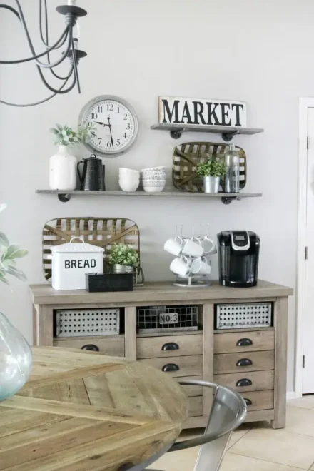 Farmhouse coffee bar with a rustic console, coffee maker, mug stand, bread box, shelves with decor, and a "MARKET" sign.