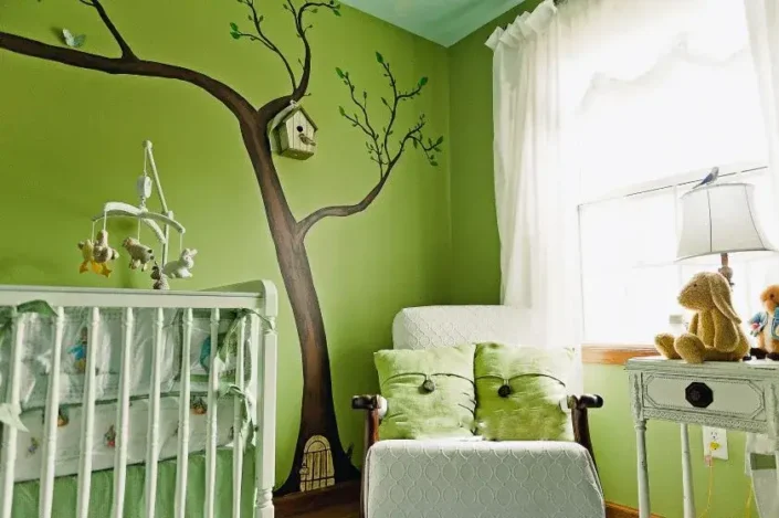 Gender neutral nursery with green-themed decor, tree mural, crib, and rocking chair—perfect for small nursery room ideas.