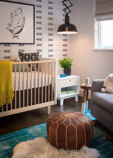 Modern, cozy gender neutral nursery design with wooden crib, black and white arrow-patterned wall, and cozy decor.