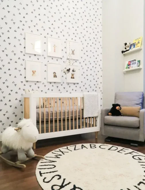 Cozy gender-neutral nursery with white crib, gray armchair, and rocking sheep toy. Animal-themed wall decor and alphabet rug enhance the small nursery design ideas.