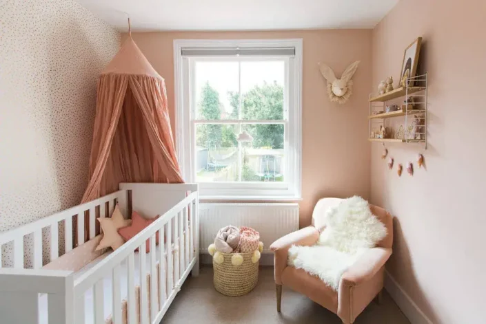 Cozy gender-neutral nursery with white crib and pink canopy, star pillows, pink armchair, and window view of garden—perfect for small nursery