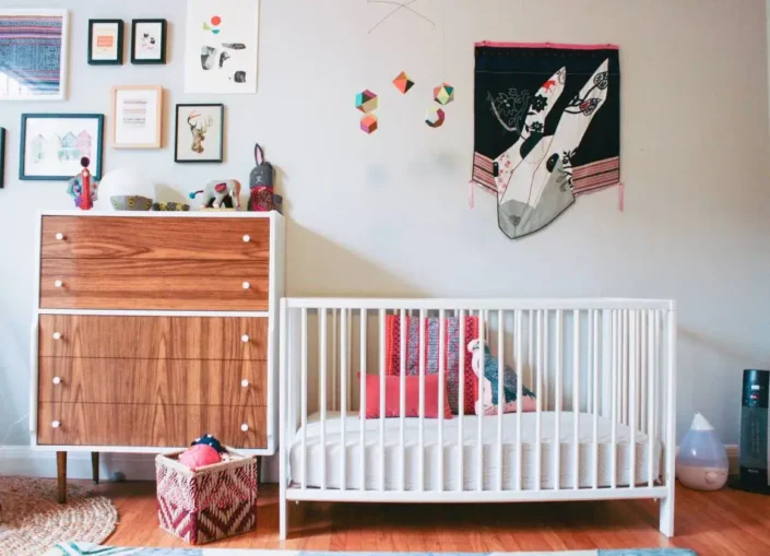 Gender-neutral nursery with white crib, colorful pillows, framed artwork, and a cozy atmosphere—ideal for small nursery