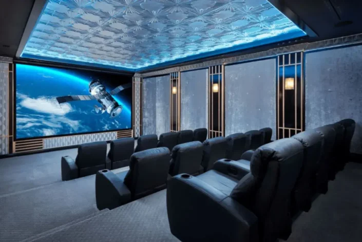 Home theater room with a large screen displaying a satellite in orbit above Earth, starry sky ceiling lighting, dark reclining seats, and concrete-textured walls, creating an immersive space-themed viewing experience perfect for basement home theater