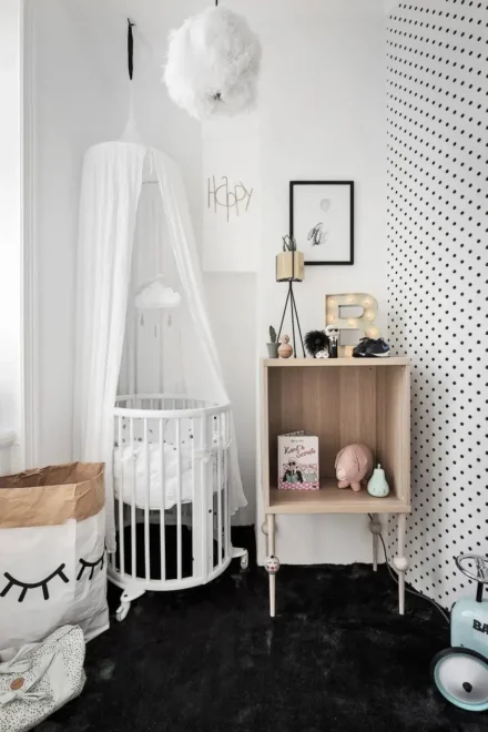 Gender-neutral nursery with circular crib, canopy, cloud mobile, and polka dot wall. Ideal for small nursery