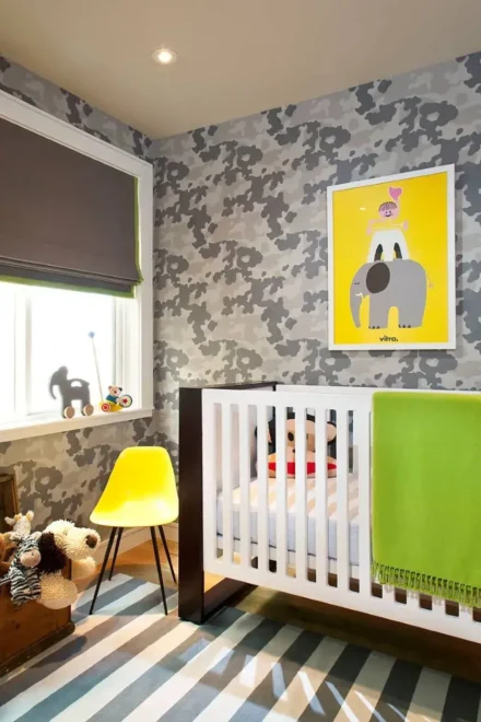 Gender-neutral nursery with a white crib, yellow chair, and wooden toy box. Gray camouflage wallpaper and striped rug complete the small nursery design