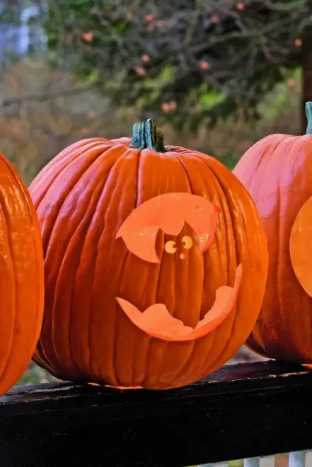 Close-up of a carved pumpkin with a smiling face, featuring triangular eyes and nose, placed on a railing, perfect for very easy pumpkin face carving ideas and traditional Halloween decorations.