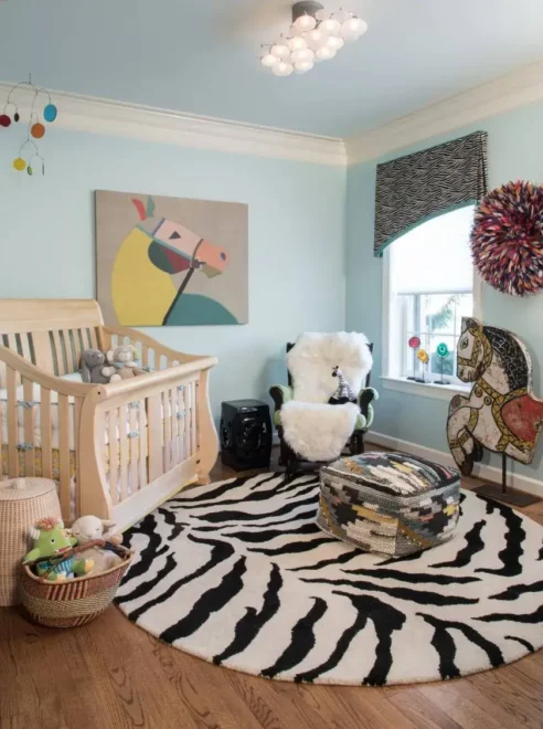 Gender-neutral nursery with wooden crib, zebra-striped rug, and animal-themed decor. Bright and cozy, perfect for neutral nursery