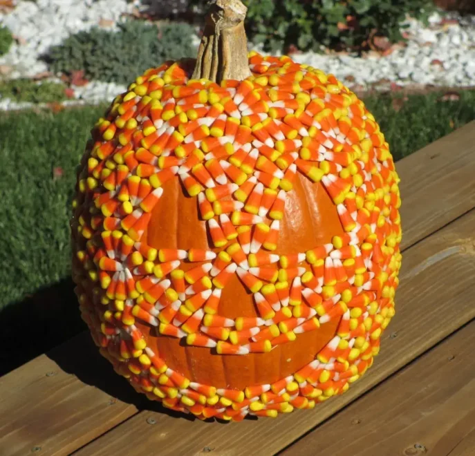 Pumpkin decorated with candy corn to resemble a jack-o’-lantern, set in a garden bed with white and grey pebbles, perfect for easy and creative Halloween decorations