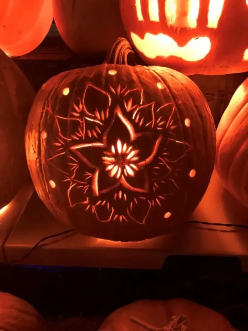 Pumpkin with an intricate floral carving, illuminated from within, creating a glowing and detailed pattern, perfect for easy but impressive Halloween decorations.