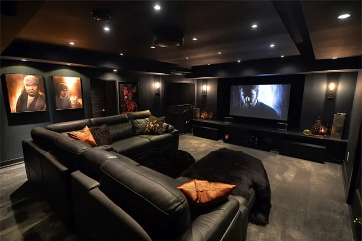 Sophisticated basement home theater room featuring a large screen, tiered black leather seating with orange and brown cushions, dark walls, recessed lighting, and framed artwork, perfect for basement movie theater seating ideas and home theater room designs