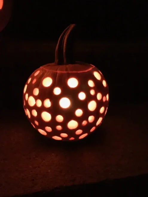 Pumpkin with circular holes illuminated from within, creating a simple yet striking pattern, ideal for very easy pumpkin face carving ideas and beginner-friendly Halloween decorations.