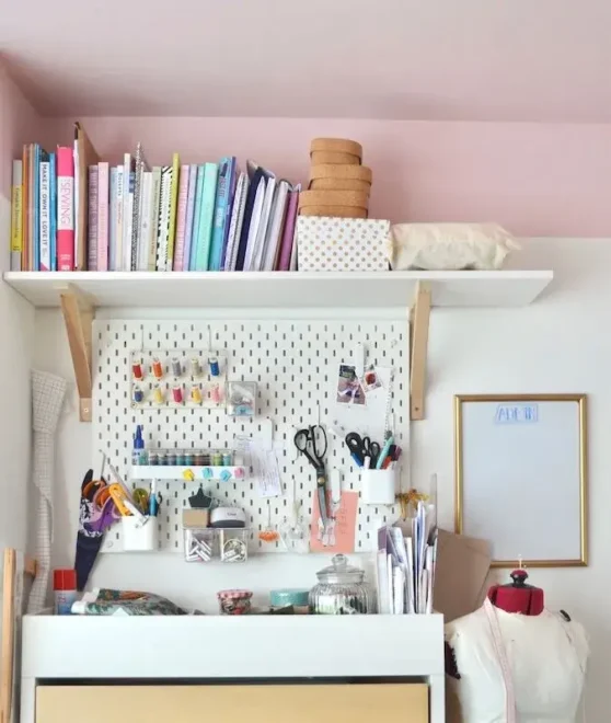 A neat and efficient craft workspace with a pegboard wall holding various sewing supplies and organized shelves for additional storage.