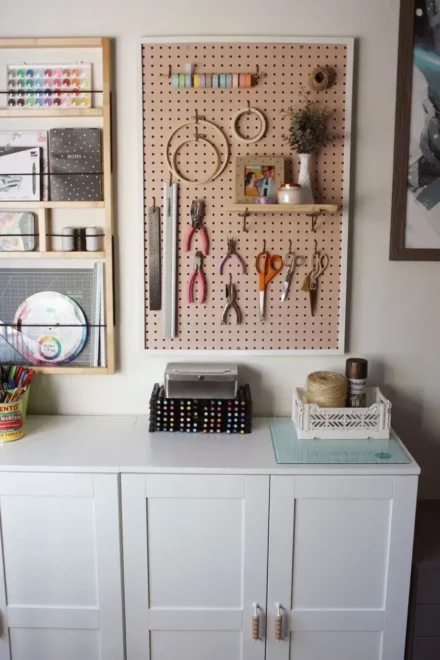 A neatly organized craft space with a white cabinet and a pegboard wall displaying various craft supplies.