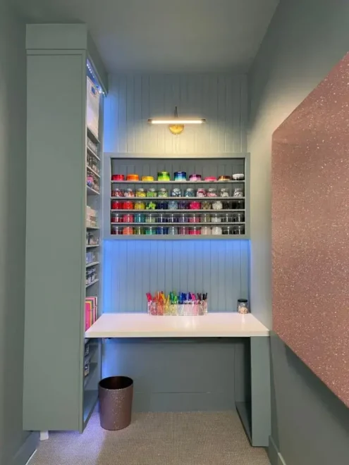 A well-organized craft workspace with a white desk, colorful markers, and shelves filled with neatly arranged craft supplies.