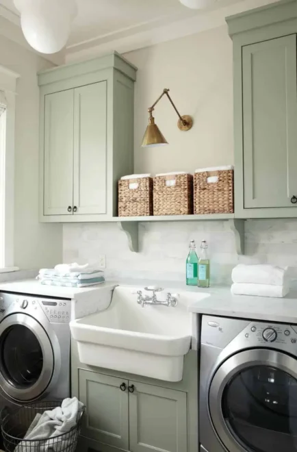 Laundry room with a white utility sink, green cabinets, brass fixtures, and silver washer and dryer.