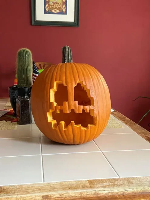 Pumpkin carving featuring a Pac-Man ghost design, placed on a tiled surface with a cactus in the background, perfect for easy and cool Halloween decorations inspired by video games.